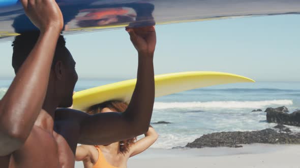 African American couple holding surfboards on their heads alt