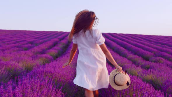 Young Woman in White Dress Walking Through a Lavender Field on Sunset