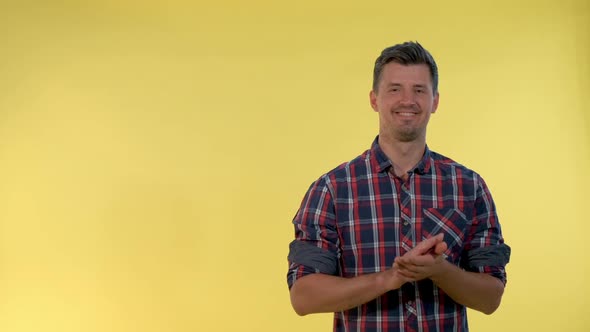 Portrait of Smiling Young Man Giving Applause To Somebody on Yellow Background. alt