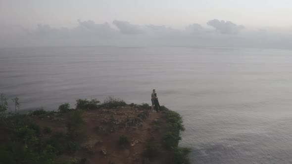 Aerial View of Couple Standing on Cliff Watching Waves on Ocean alt