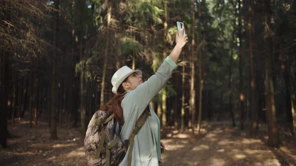 Traveler Woman in a Hat Trying To Catch a Cell Signal on the Phone in the Forest, No Signal on the alt