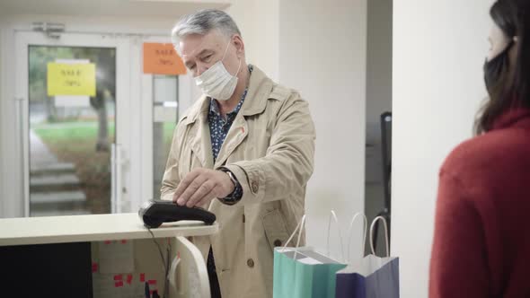 Senior Man in Covid Face Mask Using Contactless Payment in Shop. Portrait of Confident Male Customer alt