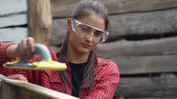 The girl with glasses works. Carpenter grinds the boards of the box alt
