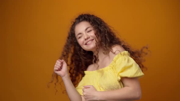 Joyful Young Woman Dancing Against Yellow Background