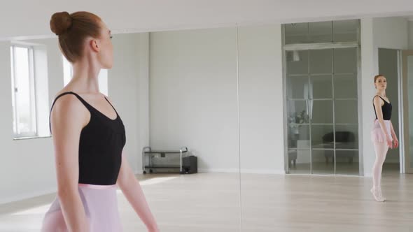 Caucasian female ballet dancer practicing ballet during a dance class in a bright studio alt