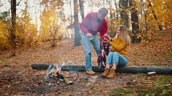 Female Frying Marshmallow on Campfire Sitting on Log in Autumn Forest alt