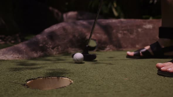 A Young Woman Playing Mini Golf. Legs in the Frame. Mid Shot. Shoot Ball in the Hole