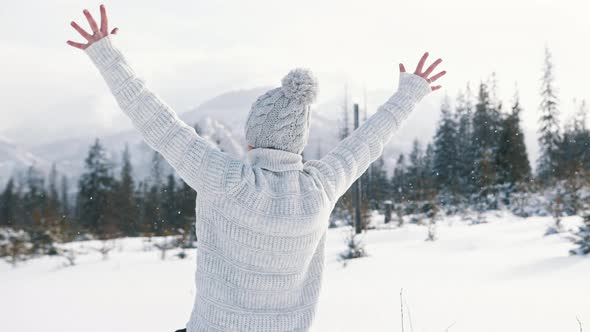 Young Woman Waching the Snowfall and Rising Her Hands on the Mountain alt