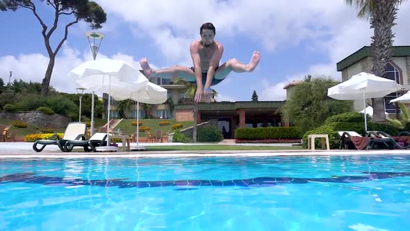 Guy is jumping into pool. Man is smiling at camera. Splash. Slow motion.