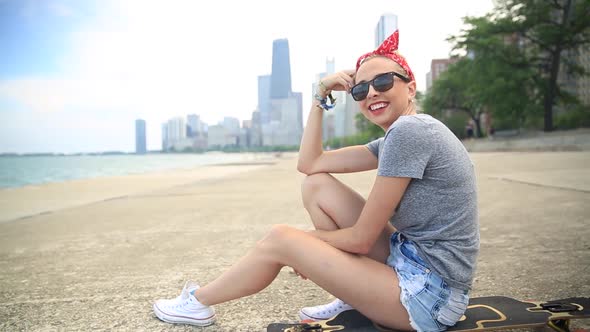 A young woman goes longboard skateboarding with the Chicago, Illinois skyline in the background. alt