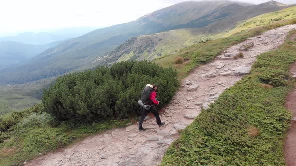 Aerial View of a Traveler with a Backpack Climbing Along Mountain Slope alt