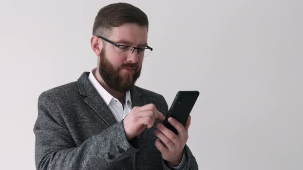 Close up view of bearded middle aged man using phone on the white wall background texting message