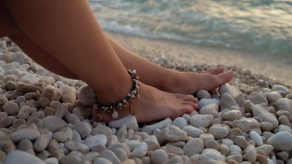 Close-up woman's legs with bracelet on pebble stones at the beach