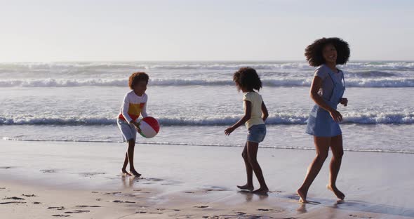 African american mother and her children playing with a ball on the beach alt