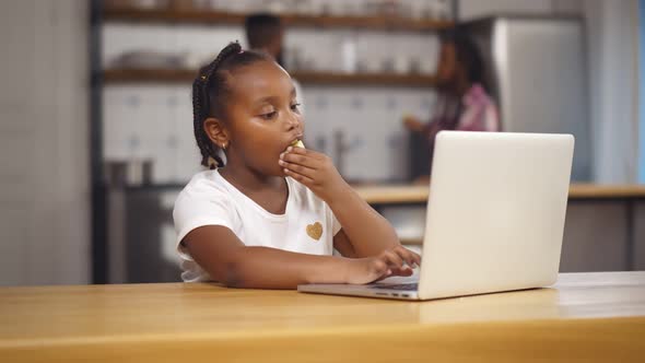 African Schoolgirl Eating Apple and Learning at Home with Laptop alt
