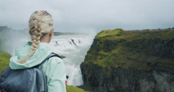 Rear View of Woman Traveler with Backpack Enjoying Gullfoss Waterfall alt