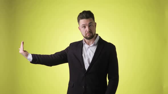Emotional Man in Office Suit Points Aside on Empty Palm on Yellow Background alt