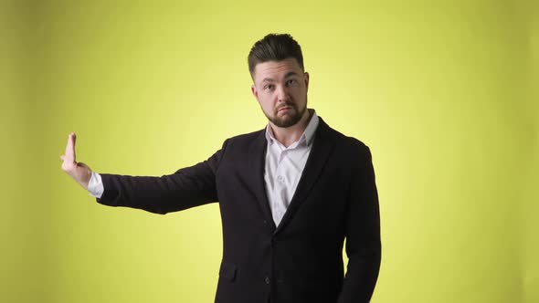 Emotional Man in Office Suit Points Aside on Empty Palm on Yellow Background