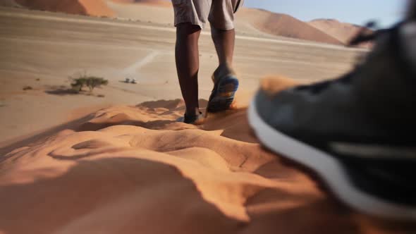 Two people walking down the famous Dune 45 in Namibia. Sand is stirred up and the shoes sink into th alt