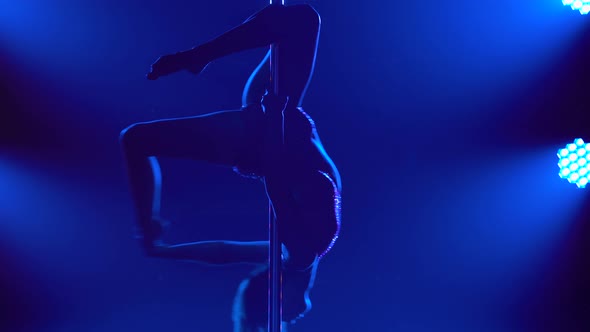 The Dancer Spins Around the Pole Upside Down in a Dark Studio alt