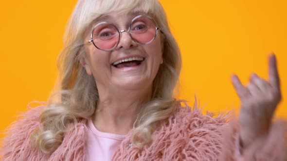 Positive Granny Showing Rock N Roll Hand Sign on Bright Background, Feeling Cool alt