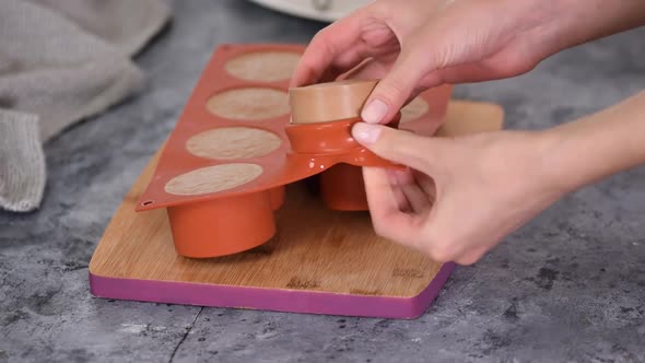 Girl takes out frozen chocolate cake blanks from a silicone mold. Close up.