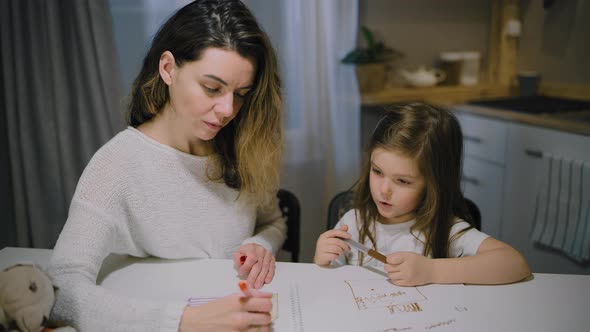 A Mother and a Small Daughter Draw Drawings on Paper in the Kitchen with Markers