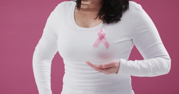 Mid section of woman with pink ribbon on her chest holding invisible object against pink background alt