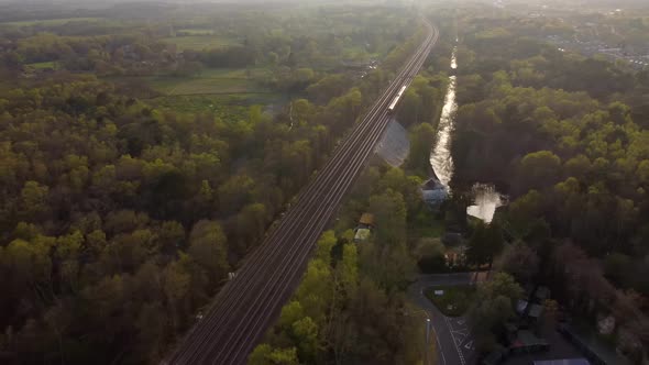 Beautiful aerial view of train travelling at sunset with forest and fields alt