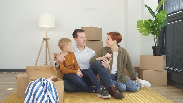 Happy Family Sitting on the Floor in a New Apartment Discussing Further Plans