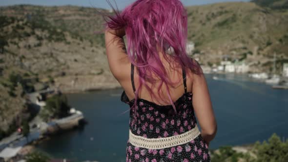 Girl with Tousled Pink Hair in a Dress with a Floral Print Looks at the Water