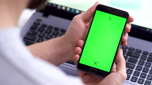 A Black Smartphone with Green Screen for Chroma Key Compositing the Hands of a Man on Laptop