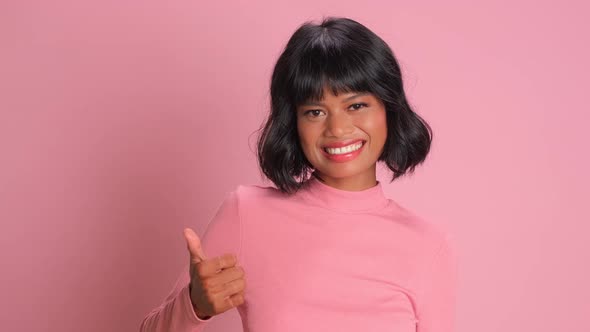 Lovely Mixed Race Young Woman Makes Thumb Up Gesture Approves Ok Over Pink Wall alt