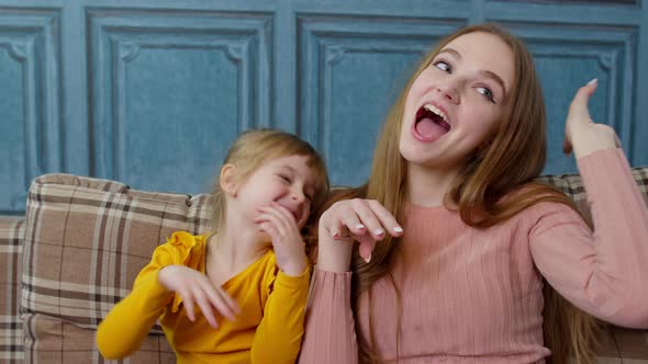 Mother and Little Child Kid Daughter Having Fun Sitting on Sofa Ooling Around Making Faces at Home alt