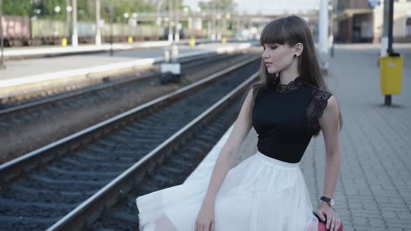 Thoughtful Lady in Blackwhite Dress Sitting in Poses on Suitcase at Railway alt