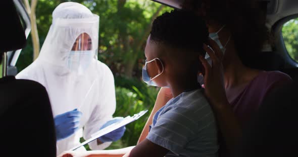 African american mother and son sitting in car having covid test done by medical worker outdoors alt
