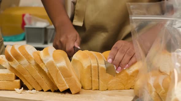 A female chef slicing loaf of bread on a wooden board in the culinary kitchen. 