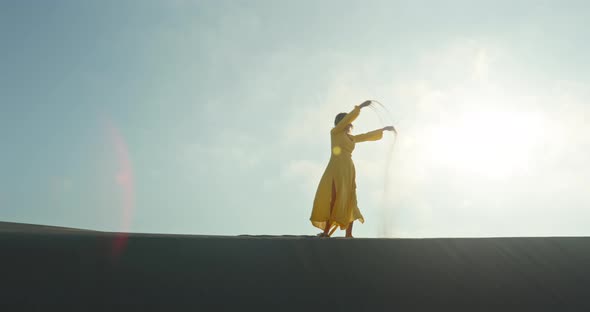 Stylish Woman in Yellow Dress Walking on Top of Sand Dune in Slow Motion alt