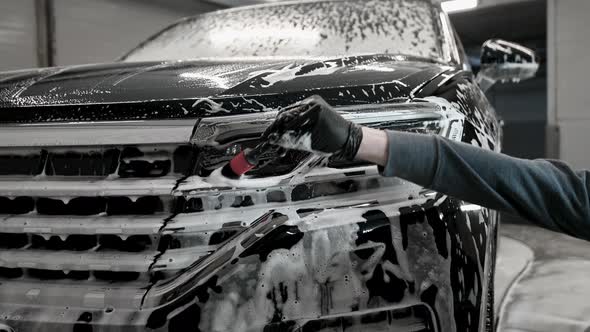 A Man in Gloves Cleans the Headlights of the Car with a Special Brush alt