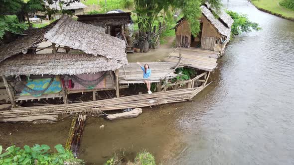 Aerial view of a beautiful young asian woman waving hand by the river in rural village by drone