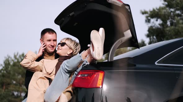Husband and Wife Sit on Car Trunk and Cuddle in Nature alt