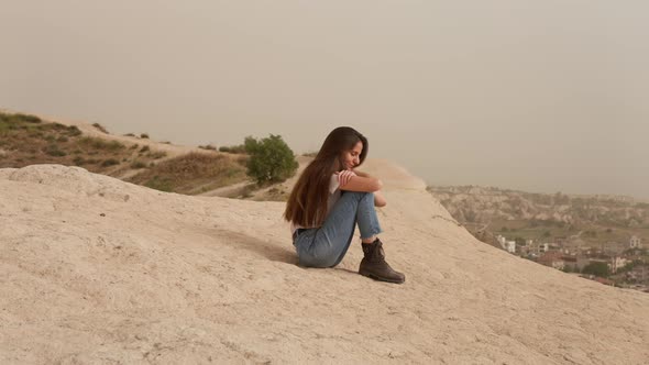 Woman Sitting on Mountain Slope Above Town