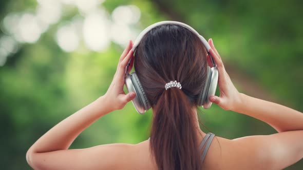 Happy asian woman adjusting wireless headphones before starting jogging and listening to music