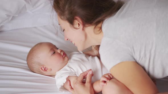 Loving Young Mommy Hugging Soothing Adorable Sweet Baby Girl Lying in Bed alt