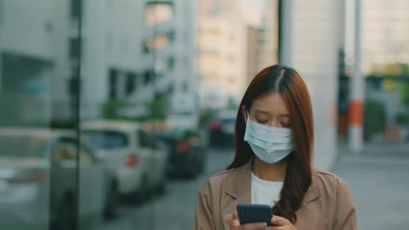 Asian businesswoman wearing medical mask walking in the street and using a smartphone