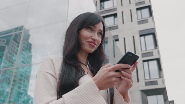 Smiling Business Woman Texting Messages on Smartphone Outdoors Near Big Modern Building