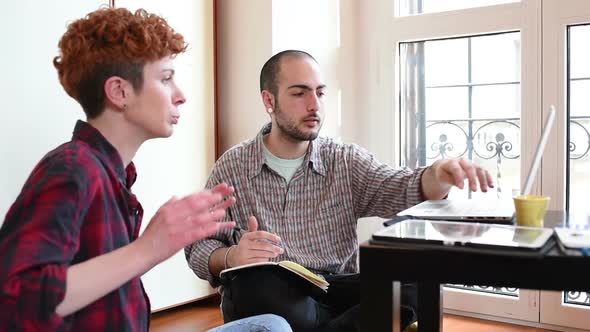 Two young beautiful man and woman working indoor in house using computer, talking to each other alt