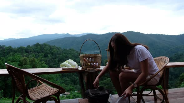 A woman preparing and putting charcoal into a stove before cooking Moo Kata