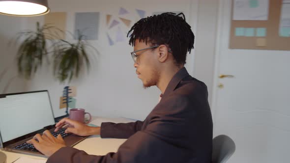 African American Man Typing on Laptop in Office during Workday alt
