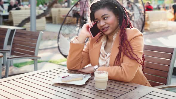 African American Woman Sitting in Outdoor Cafe and Talking on the Phone